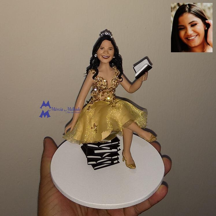 Boneca de aniversário 15 anos com vestido dourado sentada e lendo livros