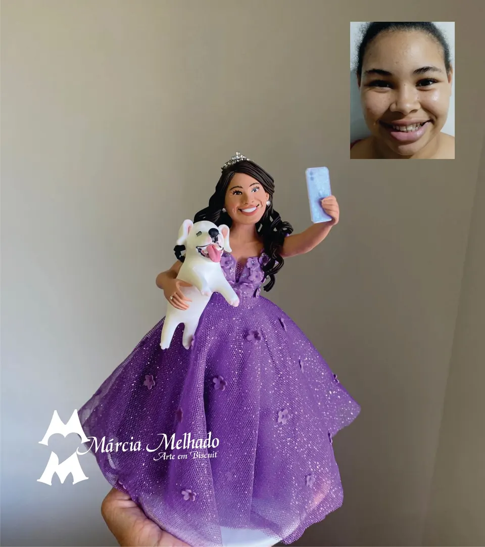Boneca com vestido lilás de tule, tiara, cachorro no colo e celular Boneca de biscuit de tiara e vestido lilás de tule com flores, segurando um cachorro branco e tirando selfie com o celular