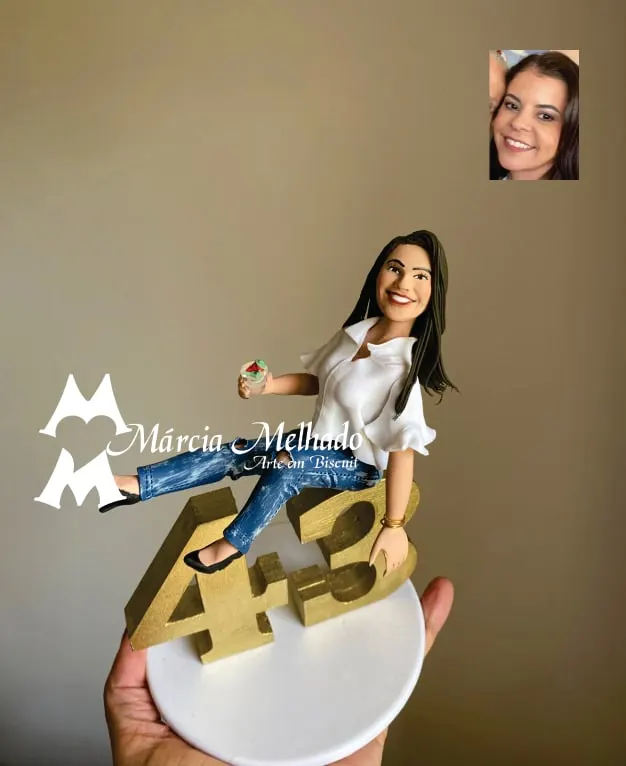 Boneca de aniversário 43 anos sentada nos números dourados Boneca de biscuit de blusa branca e jeans sentada sobre o número 43 dourado segurando um copinho, em base branca