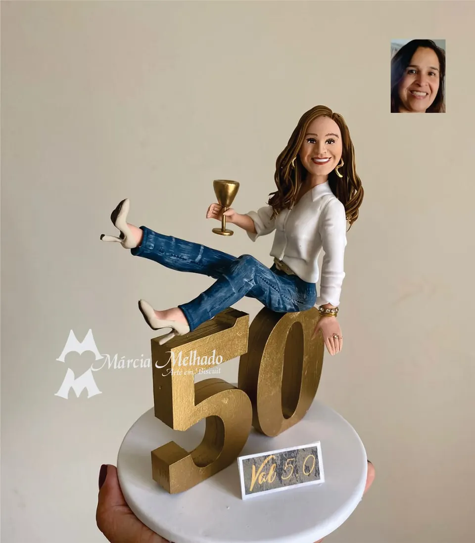 Boneca de aniversário 50 anos sentada no número dourado com taça Boneca de biscuit de camisa branca e jeans sentada sobre o número 50 dourado, com taça dourada e salto alto nude