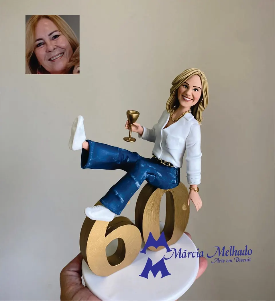 Boneca de aniversário 60 anos com camisa branca e jeans sentada no número Boneca de biscuit loira de camisa branca e jeans sentada no número 60 dourado brindando com taça dourada