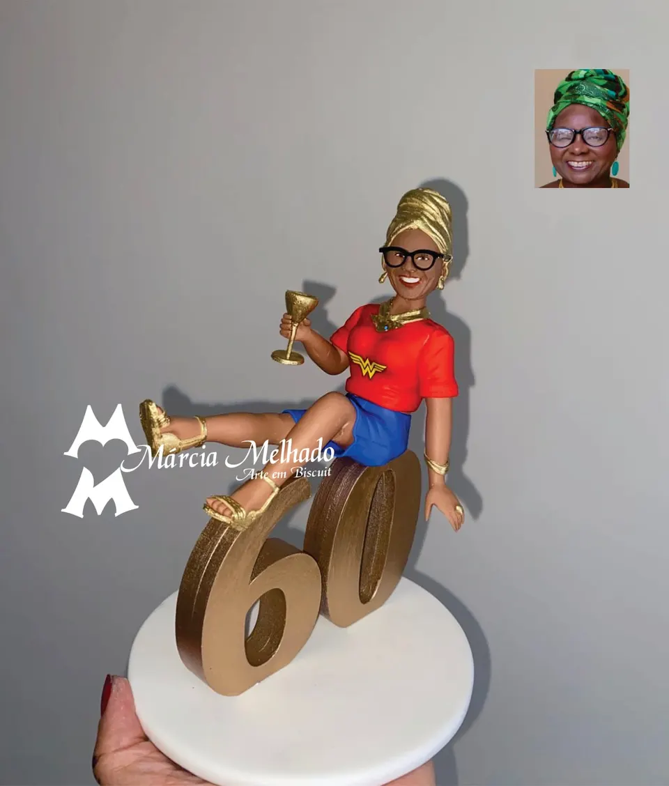 Boneca de aniversário 60 anos com camiseta da Mulher Maravilha e turbante Boneca de biscuit com turbante dourado, óculos e camiseta da Mulher Maravilha, com taça na mão, sentada no número 60 dourado