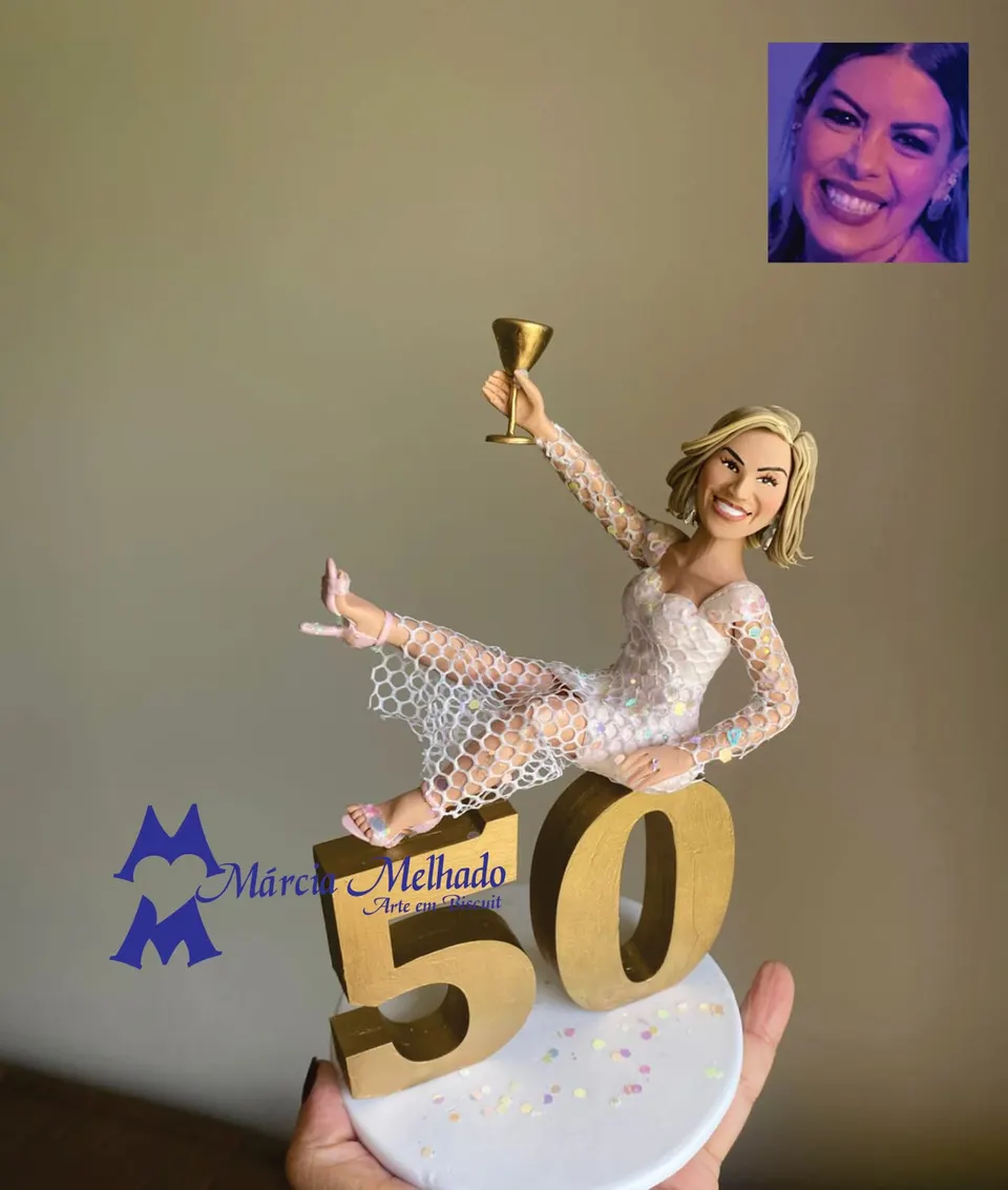Boneca de aniversário de 50 anos deitada no número com taça Boneca de biscuit loira de macacão de paetês deitada sobre um número 50 dourado, erguendo uma taça, com confetes na base