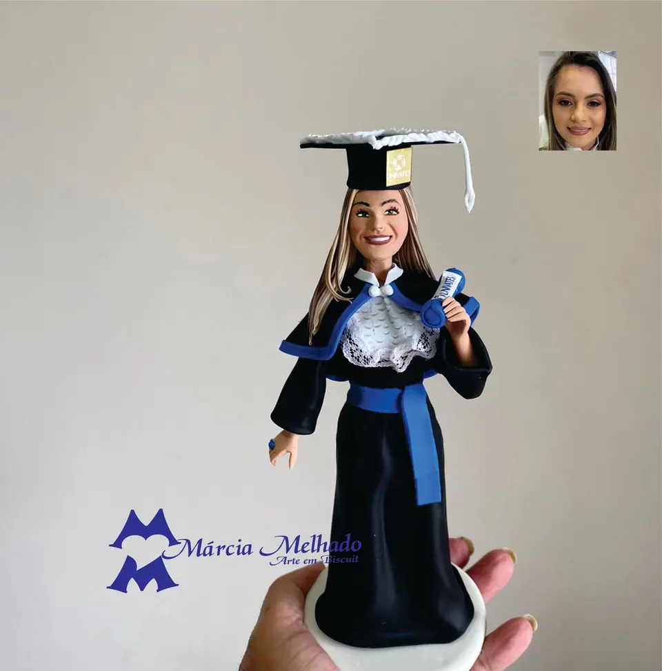 Boneca de formatura com beca preta, faixa azul e capelo Boneca de biscuit de formanda com capelo, beca preta com capa, faixa azul na cintura e canudo de diploma azul na mão