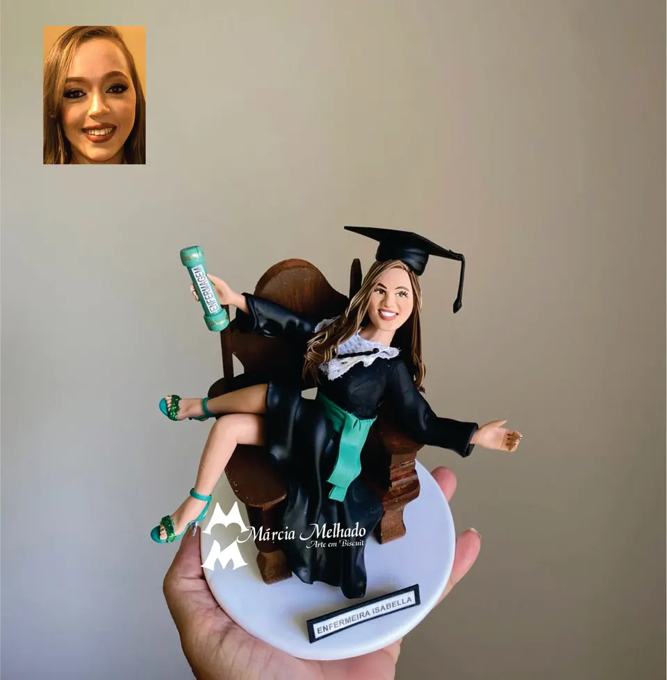 Boneca de formatura de Enfermagem sentada em cadeira de madeira Boneca de biscuit de formanda de Enfermagem com beca preta e faixa verde, sentada em cadeira de madeira com o diploma na mão