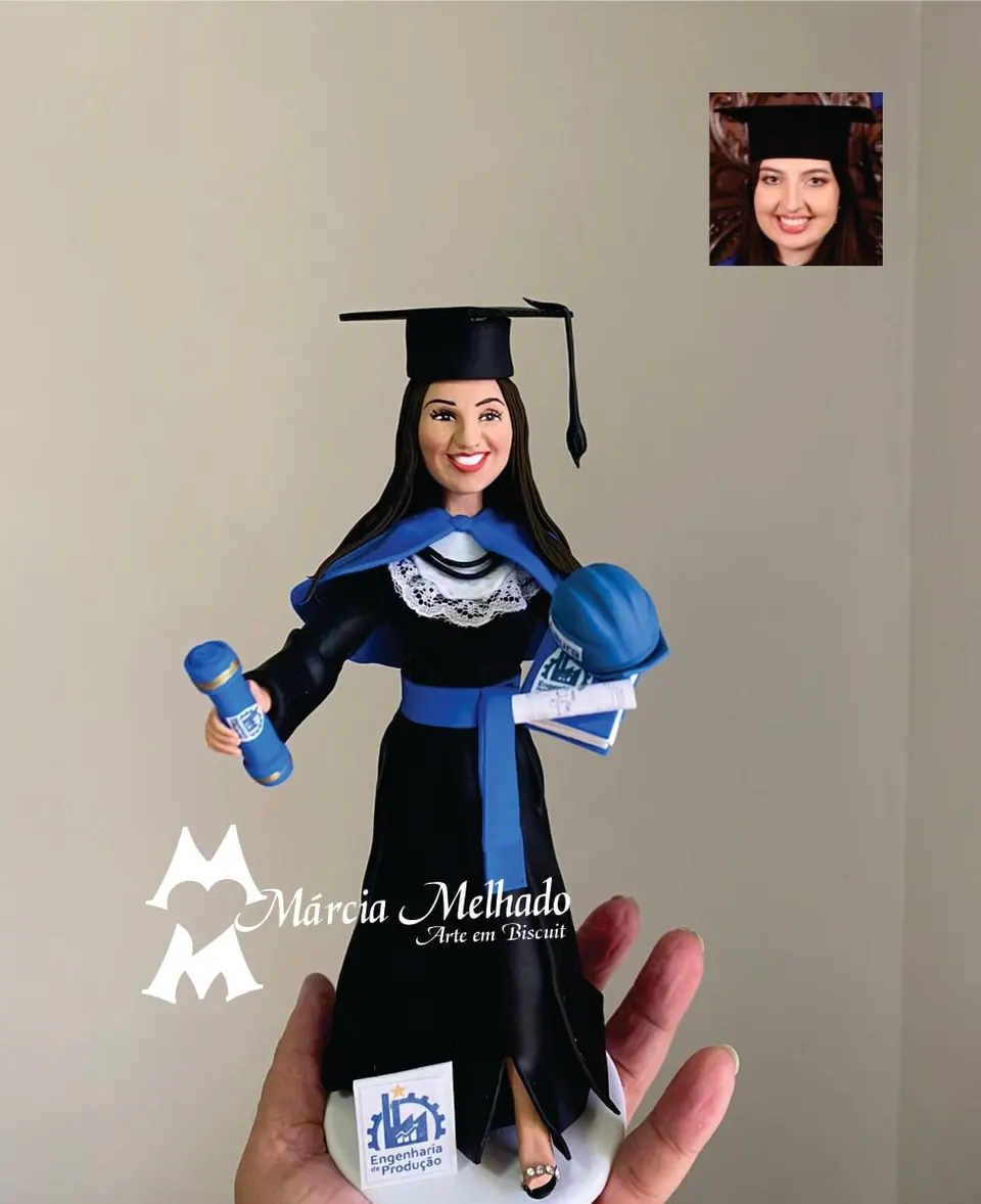 Boneca de formatura em engenharia de produção com capacete e livros Boneca de biscuit de formanda em engenharia de produção com beca preta, faixa azul, canudo, capacete azul e livros