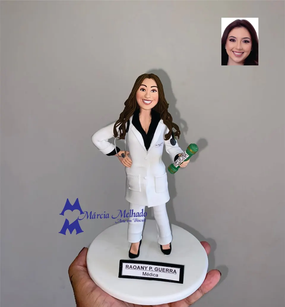 Boneca de formatura em medicina com jaleco e canudo Boneca de biscuit de médica com jaleco branco, estetoscópio e canudo verde de Medicina na mão, em pé sobre base branca