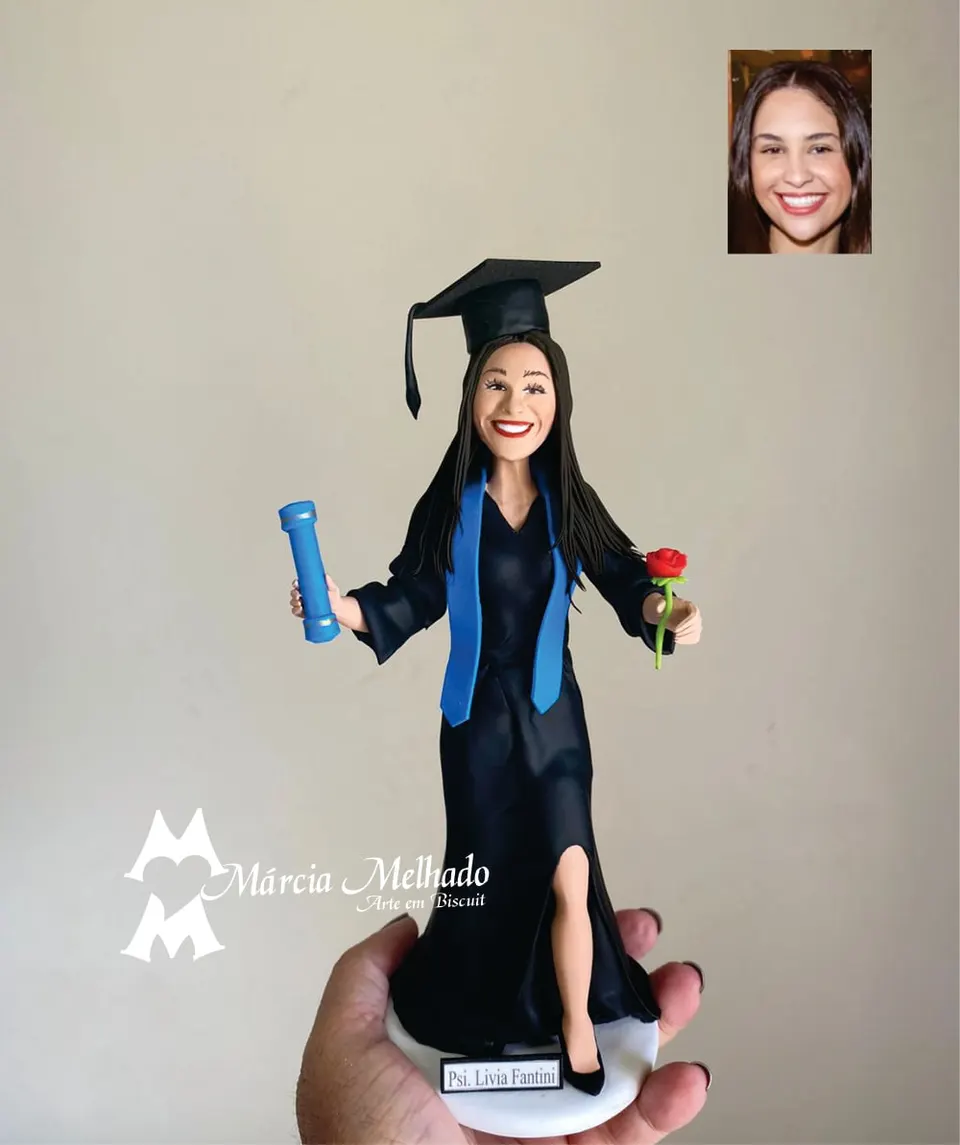 Boneca de formatura em psicologia com diploma e rosa Boneca de biscuit formanda de beca preta, capelo e faixa azul, com canudo de diploma azul e rosa vermelha nas mãos