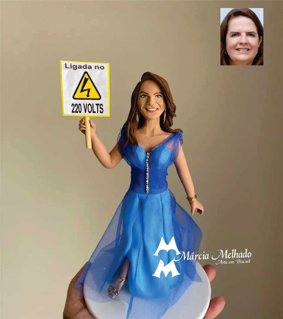 Boneca de vestido azul com placa ligada no 220 volts Boneca de biscuit de vestido azul de tule segurando uma placa amarela de alta tensão com a frase ligada no 220 volts