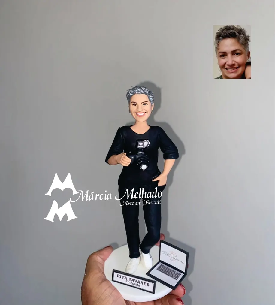 Boneca fotógrafa com câmera, notebook e plaquinha Boneca de biscuit de fotógrafa de cabelo grisalho curto, roupa preta e tênis branco segurando câmera, com notebook na base