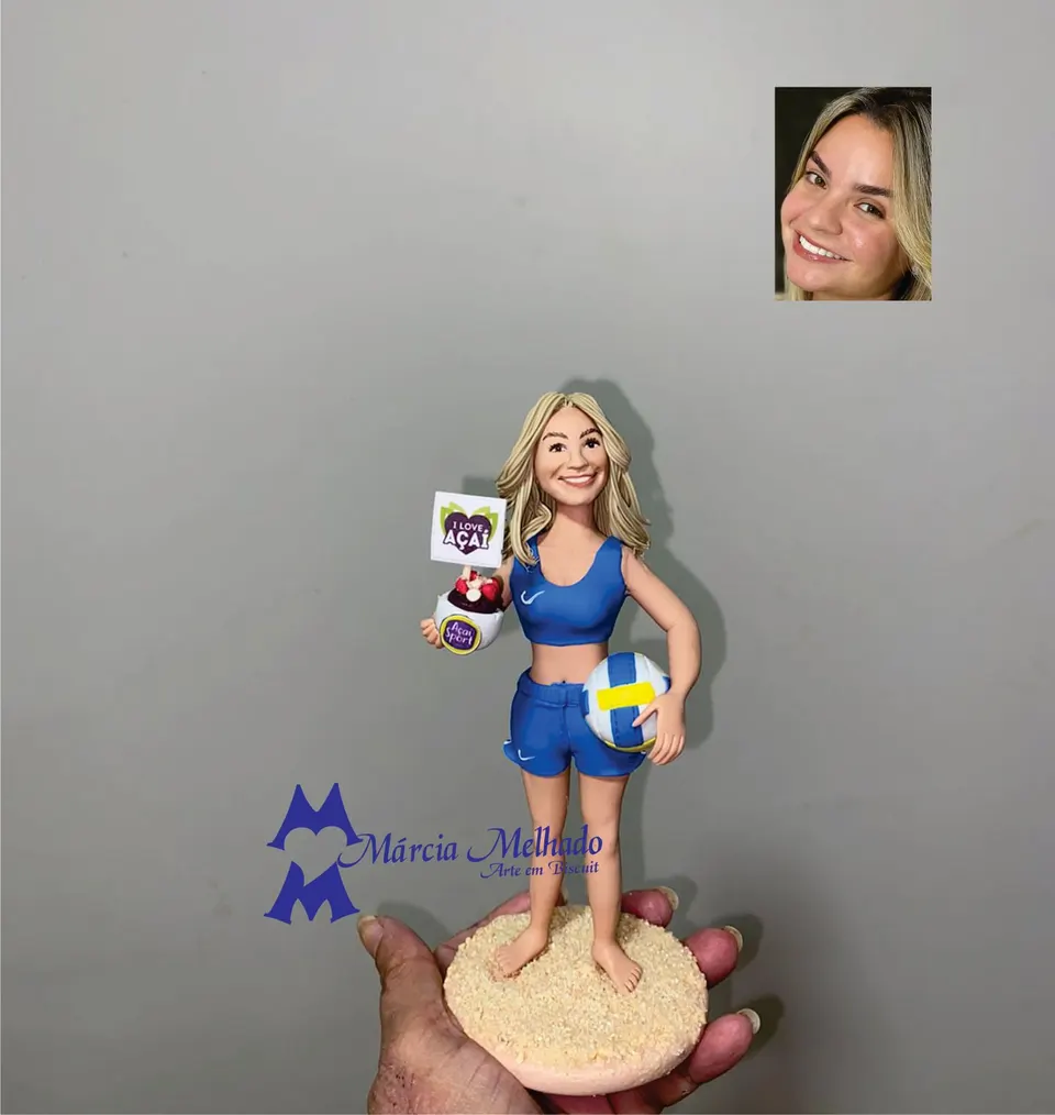 Boneca jogadora de vôlei de praia com bola e açaí Boneca de biscuit loira com uniforme azul de vôlei de praia segurando bola e pote de açaí sobre base de areia