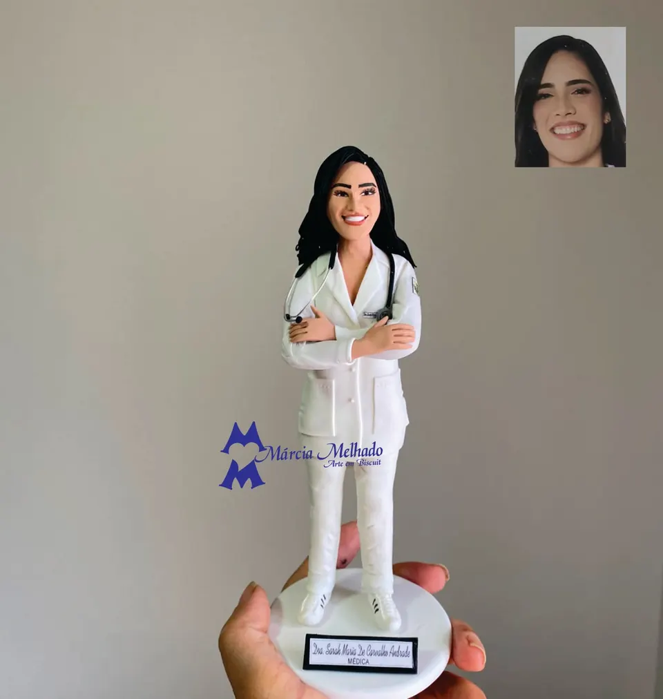Boneca médica de jaleco branco e braços cruzados com estetoscópio Boneca de biscuit de médica com cabelo preto longo, jaleco branco, estetoscópio e braços cruzados sobre base branca