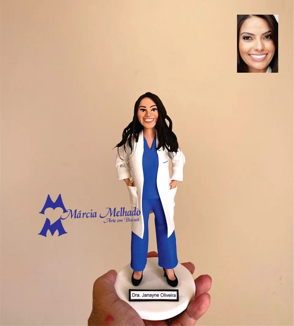 Boneca médica de jaleco branco e pijama cirúrgico azul Boneca de biscuit de médica com jaleco branco sobre pijama cirúrgico azul, estetoscópio no pescoço e mãos nos bolsos
