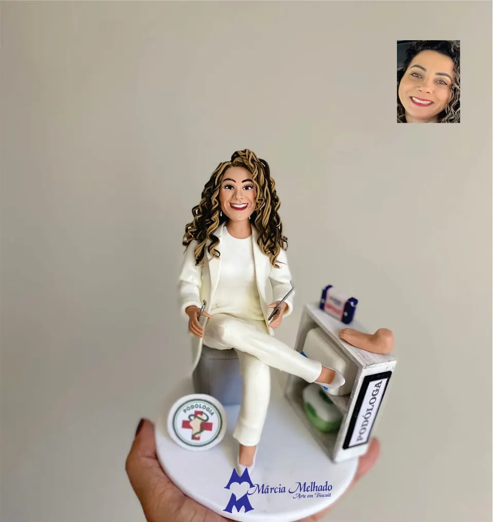 Boneca podóloga de branco atendendo um pé no consultório Boneca de biscuit de podóloga de roupa branca sentada com instrumentos nas mãos, pé apoiado na bancada e placa de podóloga