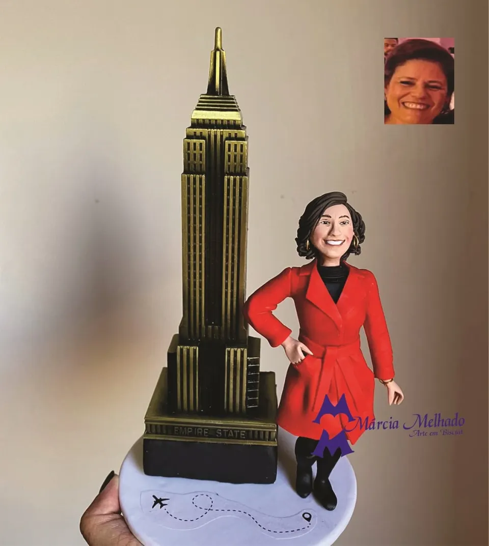Boneca viajante com Empire State Building de Nova York Boneca de biscuit de mulher com casaco vermelho e botas pretas ao lado de uma miniatura dourada do Empire State Building
