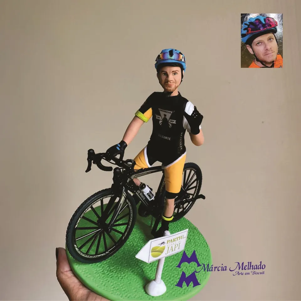 Boneco ciclista com bicicleta speed e placa Serra do Japi Boneco de biscuit de ciclista com capacete azul e camisa preta e amarela em bicicleta speed sobre base verde com placa