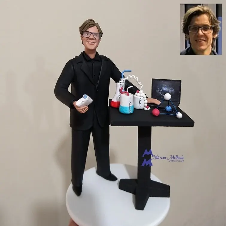 Boneco cientista químico com bancada, vidrarias e notebook Boneco de biscuit de químico com óculos de proteção e terno preto ao lado de bancada com vidrarias, molécula e notebook