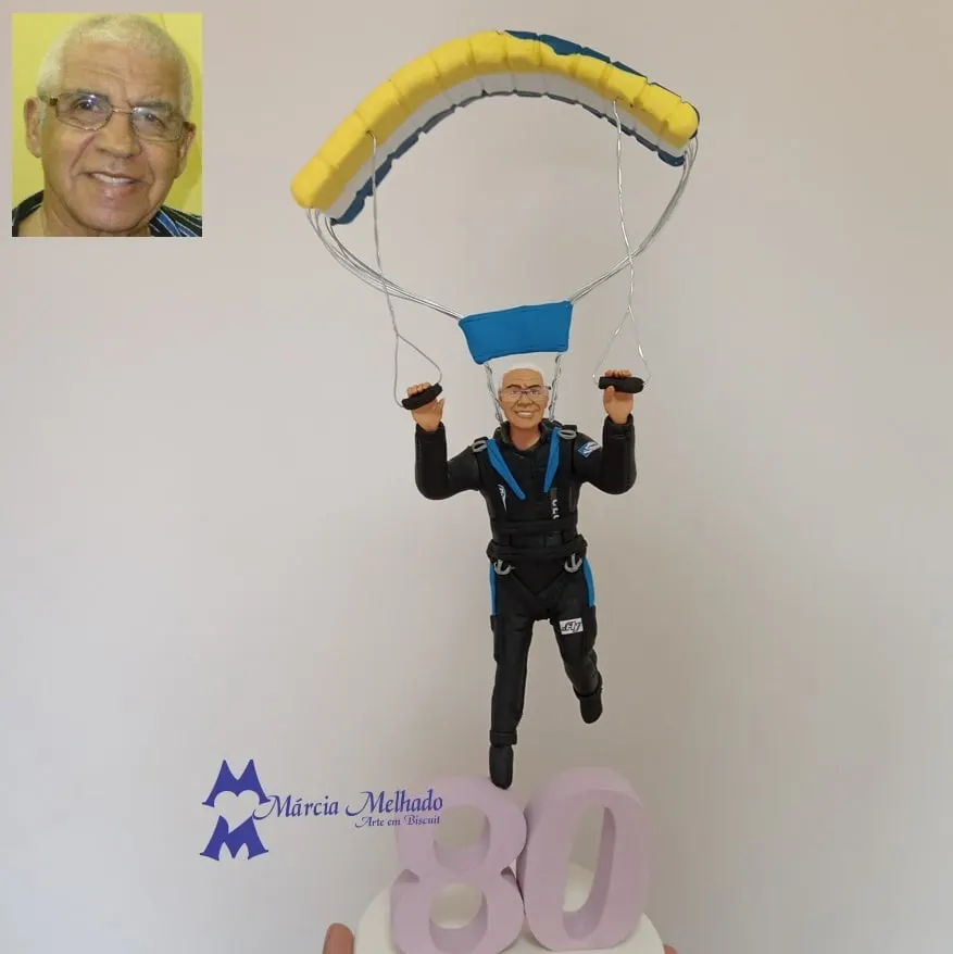 Boneco de aniversário 80 anos saltando de paraquedas Boneco de biscuit de senhor de cabelos brancos e óculos pendurado em um paraquedas amarelo e azul sobre o número 80