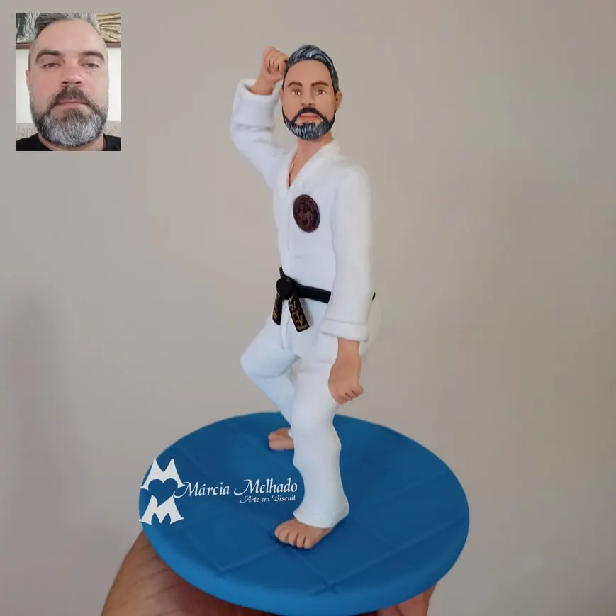 Boneco de artes marciais com kimono branco e faixa preta Boneco de biscuit de homem barbudo com kimono branco e faixa preta em pose de defesa, descalço sobre base azul de tatame