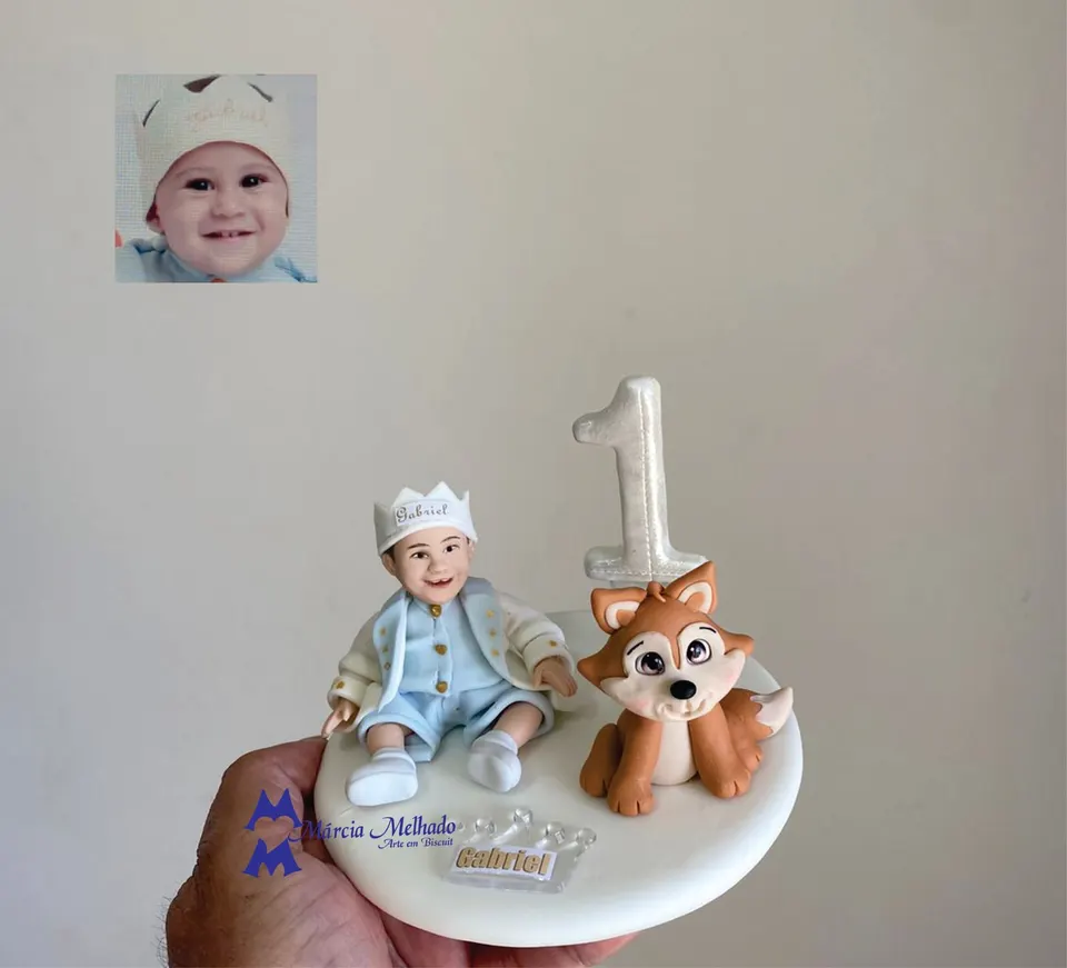 Boneco de bebê príncipe de 1 ano com raposa Bebê de biscuit sentado com coroa e roupa de príncipe azul-clara ao lado de uma raposinha e de um número 1 perolado