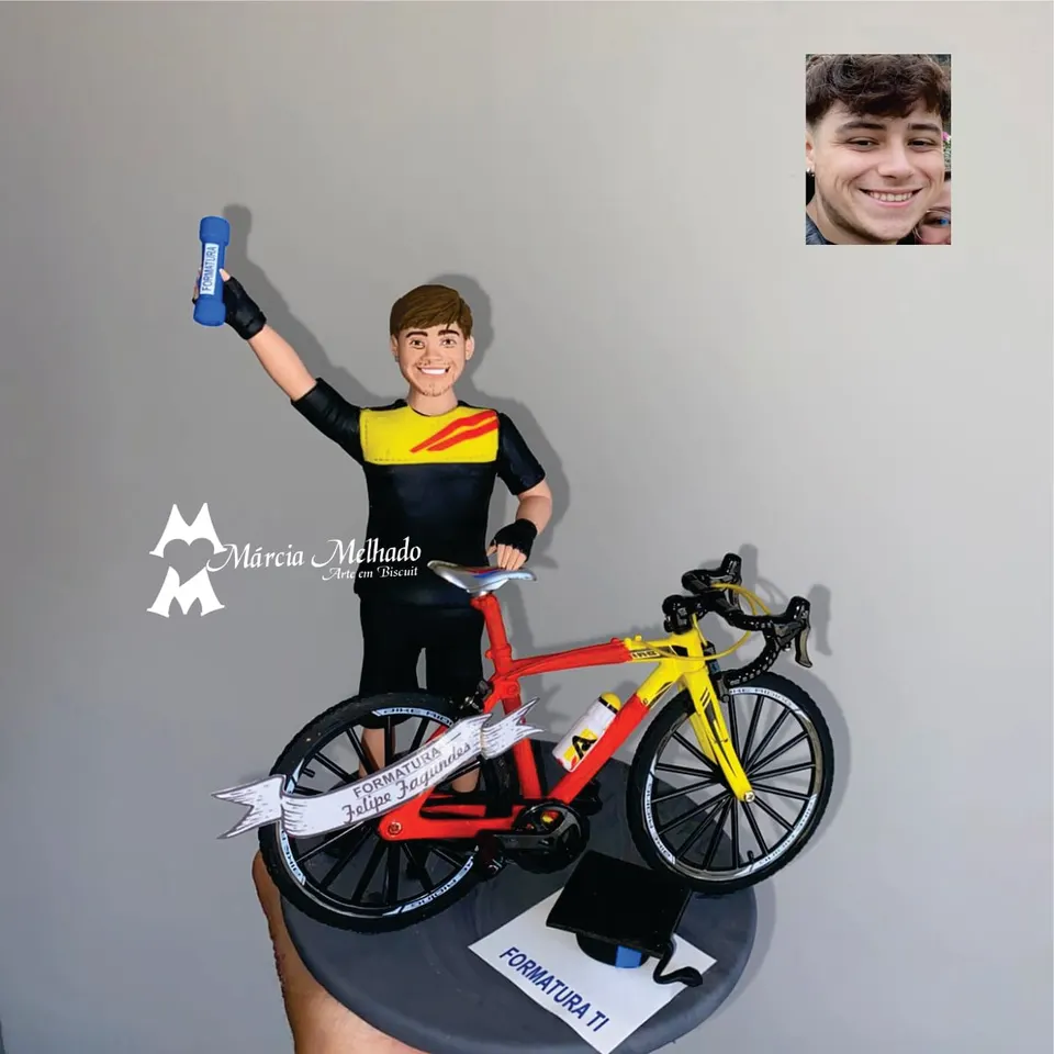 Boneco de formatura em TI com bicicleta speed e canudo Boneco de biscuit de formando com camisa de ciclismo erguendo o canudo azul, ao lado de bicicleta speed vermelha e amarela