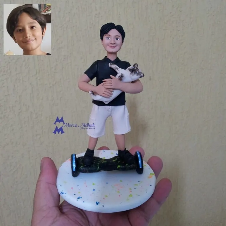 Boneco de menino no hoverboard com gato no colo Boneco de biscuit de menino de polo preta e bermuda branca em cima de um hoverboard, com um gato branco e marrom no colo