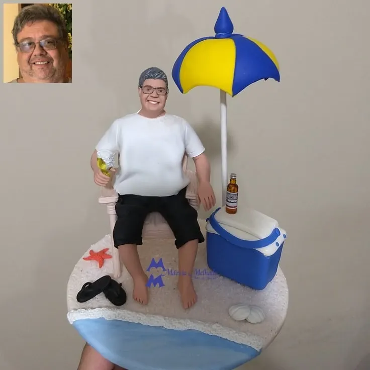 Boneco de praia na cadeira com guarda-sol, cooler e cerveja Boneco de biscuit de homem de óculos em cadeira de praia com drink, guarda-sol azul e amarelo, cooler, cerveja e chinelos