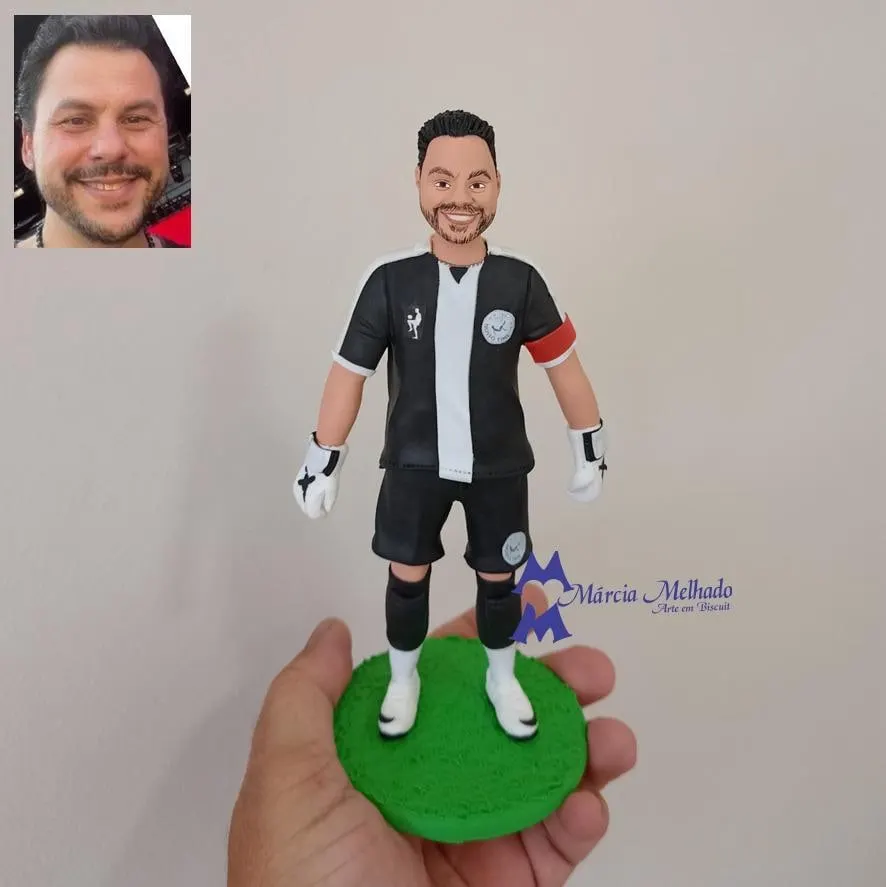 Boneco goleiro com luvas e braçadeira de capitão Boneco de biscuit de goleiro barbudo com camisa preta e branca, luvas e braçadeira de capitão em pé sobre base de grama