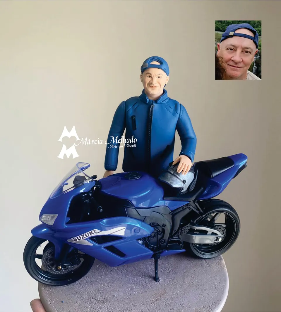 Boneco motociclista com boné e moto esportiva azul Suzuki Boneco de biscuit de homem de boné virado e jaqueta azul com a mão sobre o capacete em cima de uma moto esportiva azul Suzuki