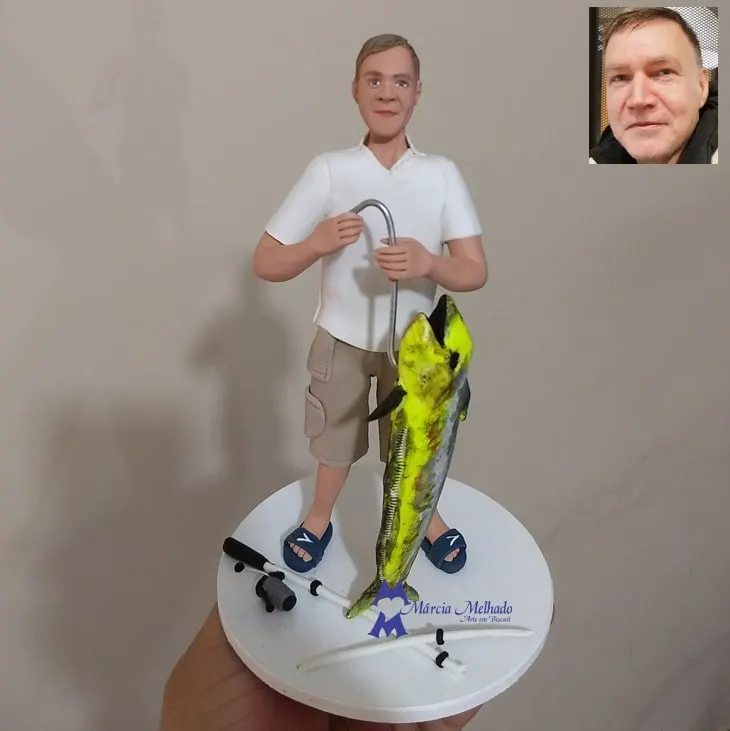 Boneco pescador com peixe dourado, anzol e vara de pesca Boneco de biscuit de pescador com camisa polo branca e bermuda segurando anzol, ao lado de um peixe dourado grande