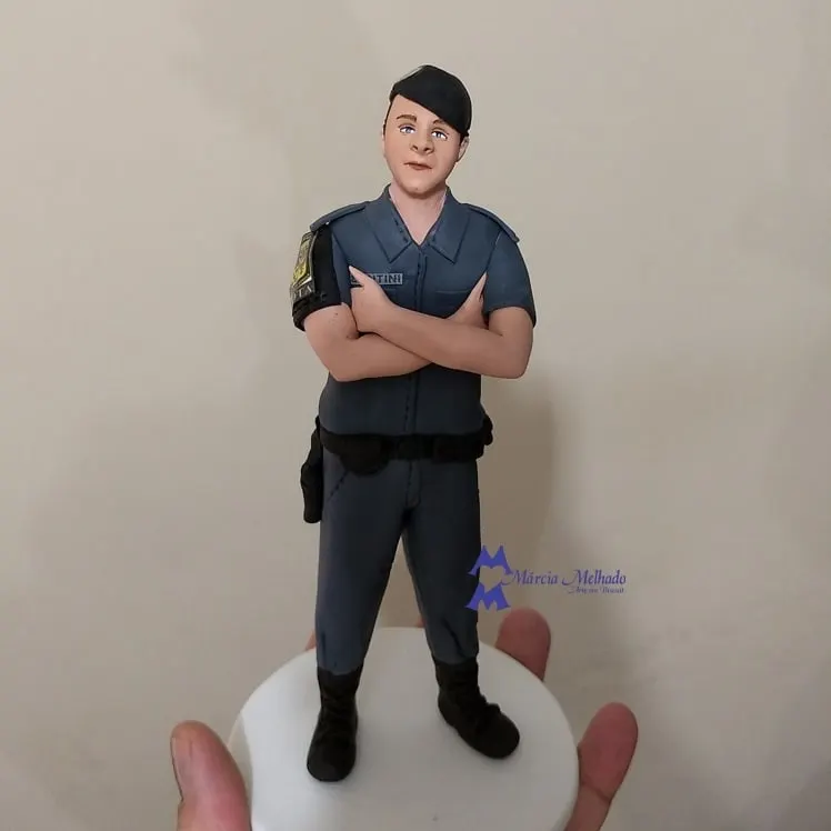 Boneco policial militar de braços cruzados com farda cinza Boneco de biscuit de policial militar com farda cinza e boina preta, de braços cruzados sobre base branca