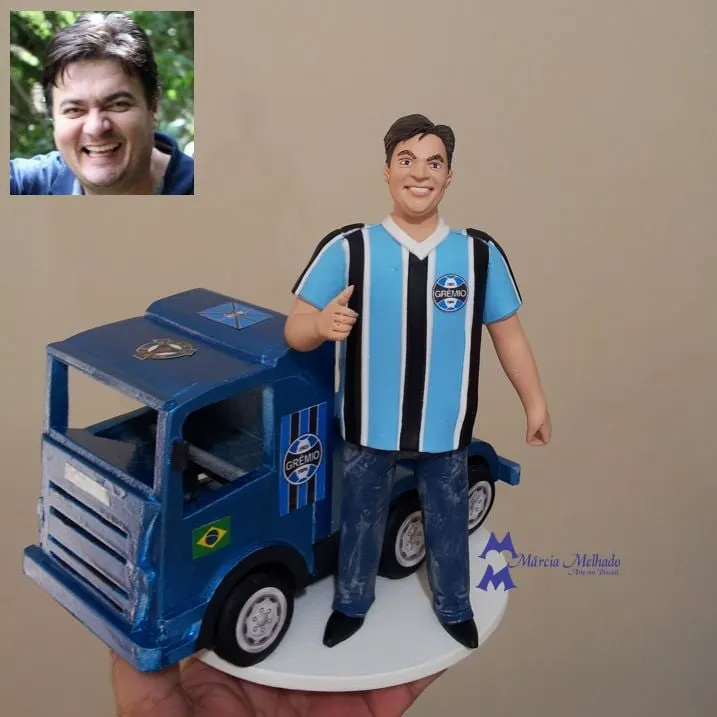 Boneco torcedor do Grêmio com caminhão azul Boneco de biscuit de homem com camisa do Grêmio fazendo sinal de positivo ao lado de um caminhão azul em miniatura