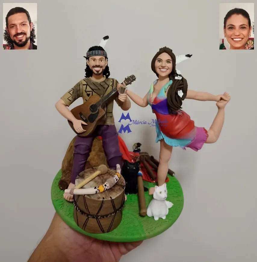 Bonecos de casal com violão, tambor e gatos em tema indígena Bonecos de biscuit de casal em tema indígena: ele toca violão com pena na cabeça, ela dança, com tambor e dois gatos na base