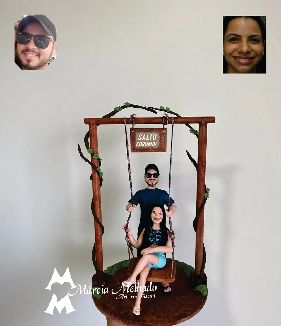 Bonecos de casal em balanço de madeira com placa Salto Corumbá Casal de biscuit em balanço de madeira com placa Salto Corumbá, ela sentada de short jeans e ele atrás de boné