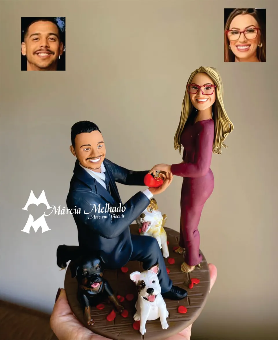 Bonecos de casal em pedido de casamento com três cachorros Bonecos de biscuit em pedido de casamento: homem ajoelhado com caixinha de aliança, mulher de macacão vinho e três cachorros