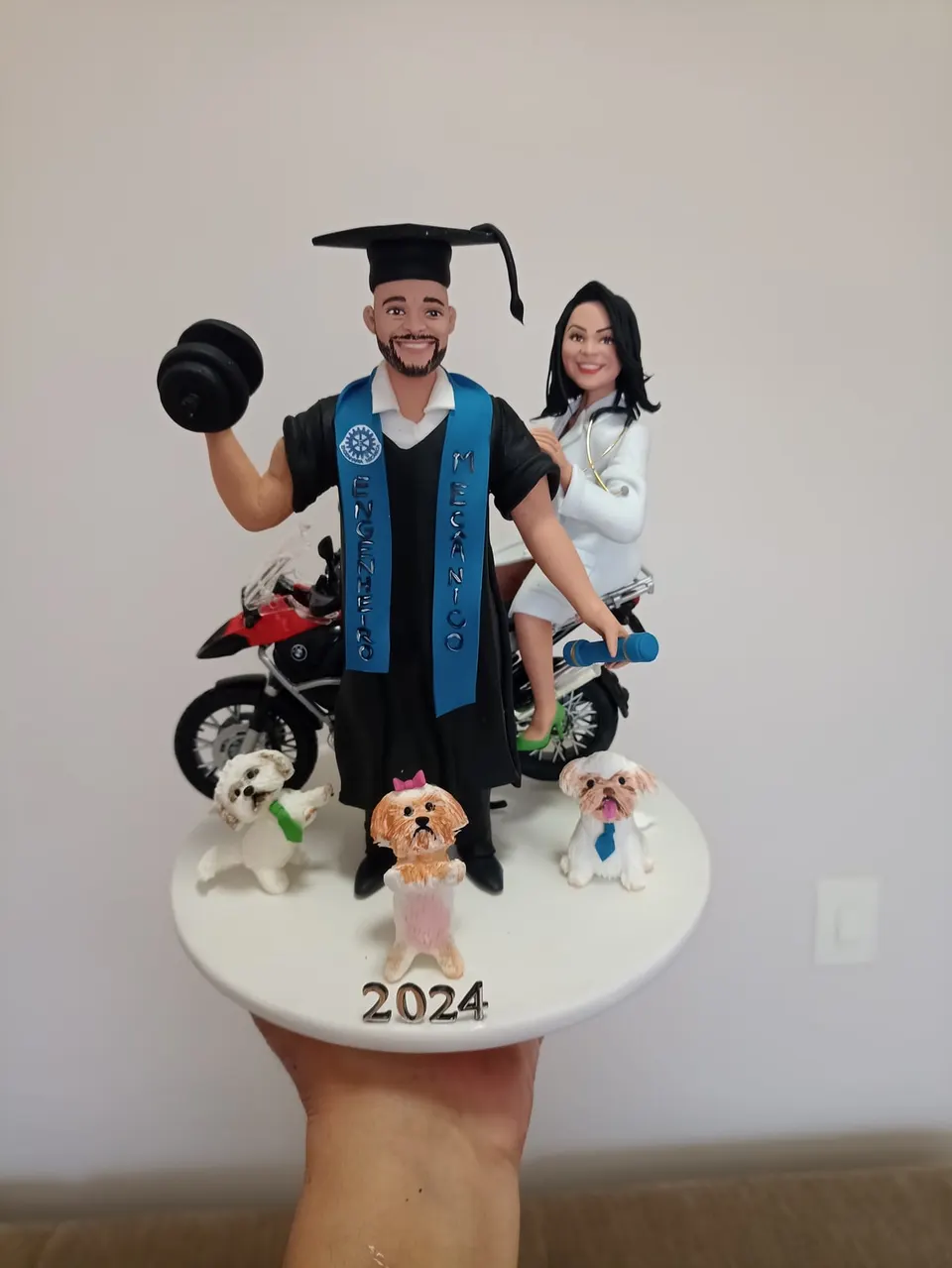 Bonecos de formatura engenheiro mecânico com moto BMW, halter e cachorros Formando de biscuit de beca e faixa de engenheiro mecânico erguendo halter, mulher de jaleco na moto BMW e três cachorros