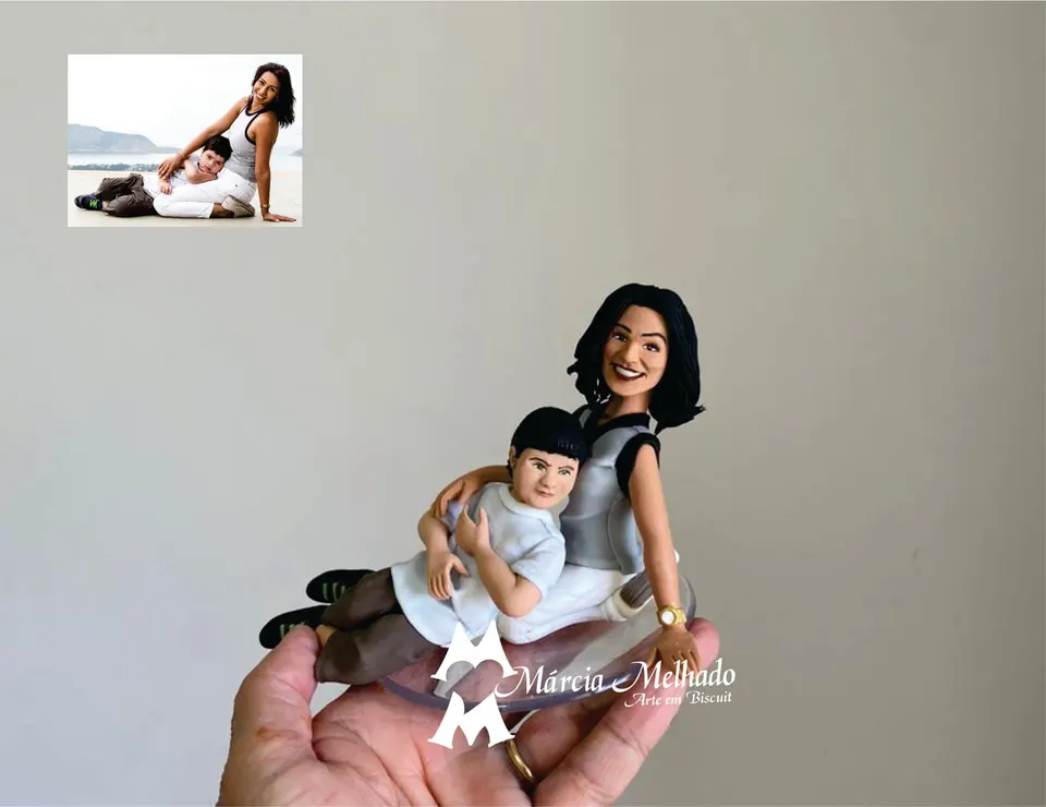 Bonecos de mãe e filho sentados com menino deitado no colo Bonecos de biscuit de mulher sentada de regata cinza e calça branca com um menino deitado no colo, sobre base transparente