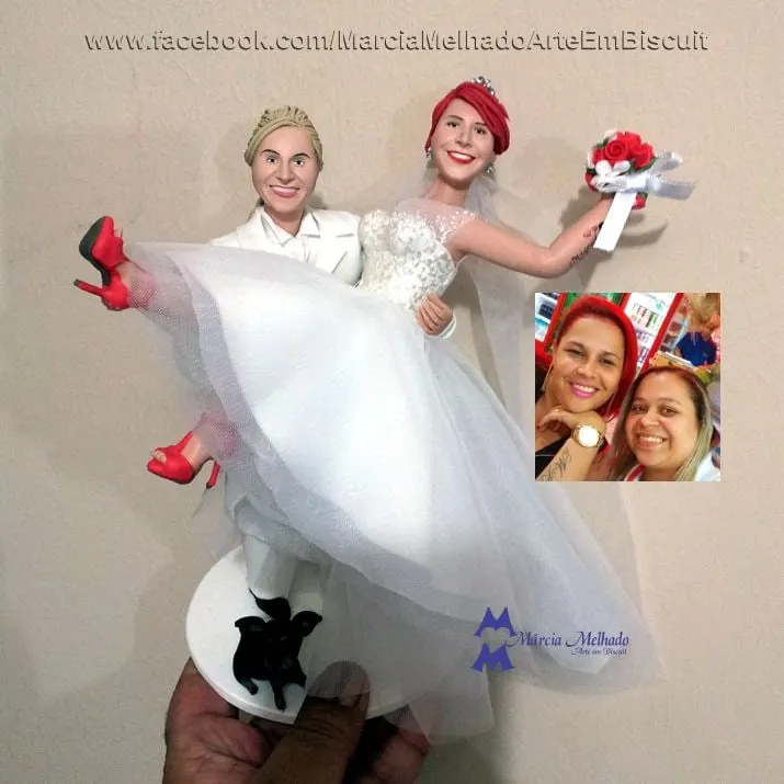 Noivinhas com noiva de terno branco carregando a outra no colo e cachorro Topo de bolo de biscuit com noiva de terno branco carregando noiva ruiva de vestido de tule e saltos vermelhos