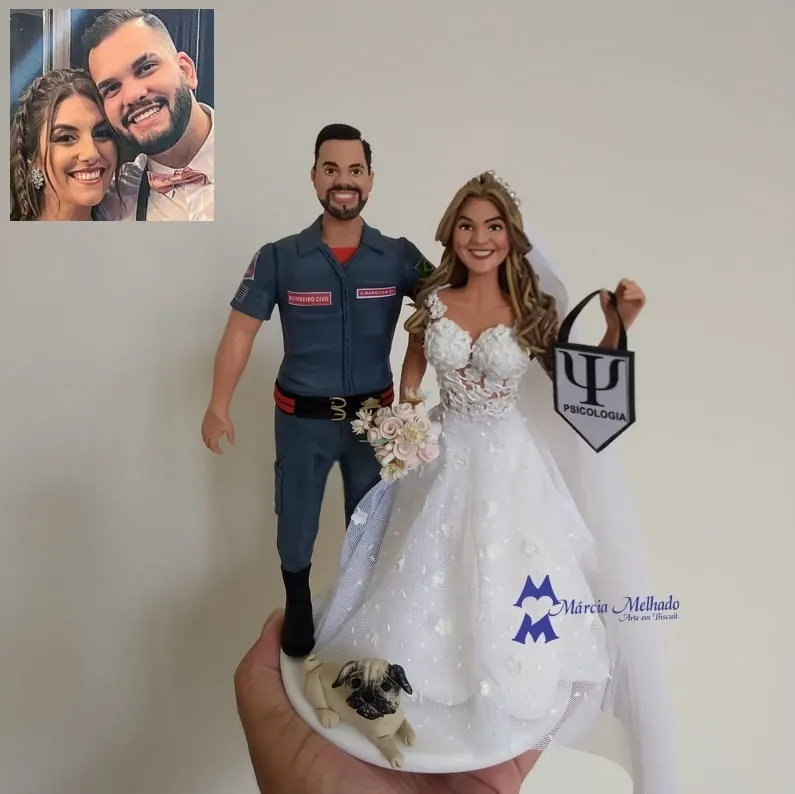 Noivinhos bombeiro civil e psicóloga com cachorro pug Noivo de biscuit com farda de bombeiro civil, noiva de vestido rendado segurando sacola de psicologia e pug na base