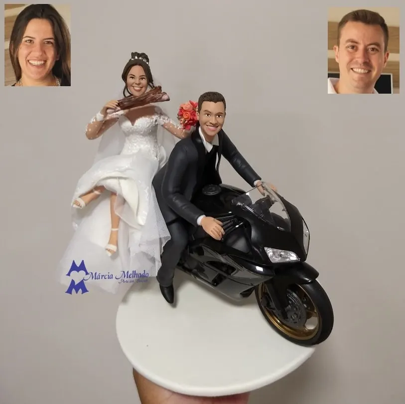 Noivinhos em moto esportiva preta com noiva segurando costela Noivinhos de biscuit em moto esportiva preta, noivo de terno pilotando e noiva na garupa erguendo uma costela e buquê