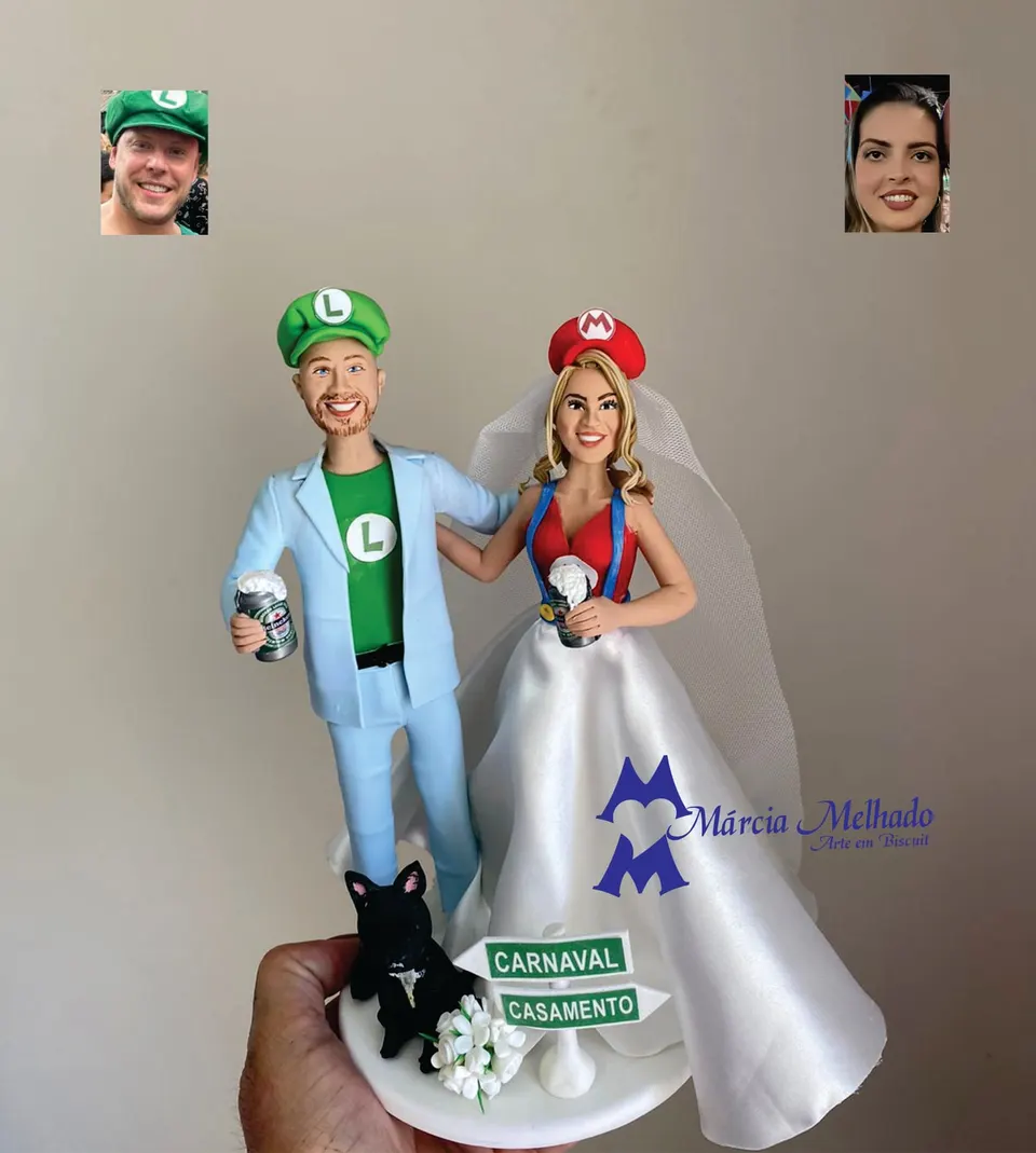 Noivinhos fantasiados de Mario e Luigi com cachorro Noivinhos de biscuit com bonés de Luigi e Mario segurando latas de cerveja, buldogue preto e placas Carnaval e Casamento