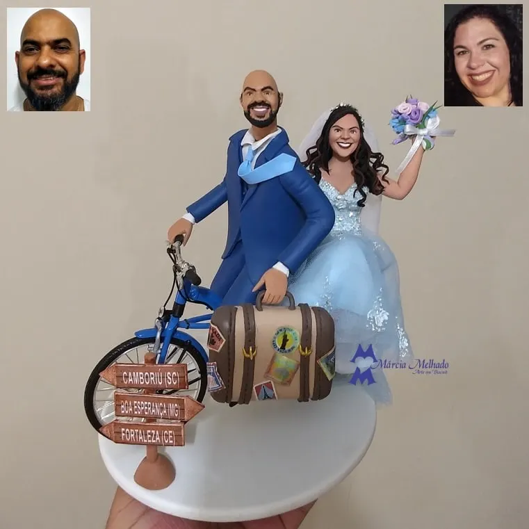 Noivinhos viajantes com bicicleta, mala de viagem e placa de destinos Noivo de terno azul em bicicleta, noiva de vestido azul-claro com buquê, mala com adesivos e placa de madeira com cidades