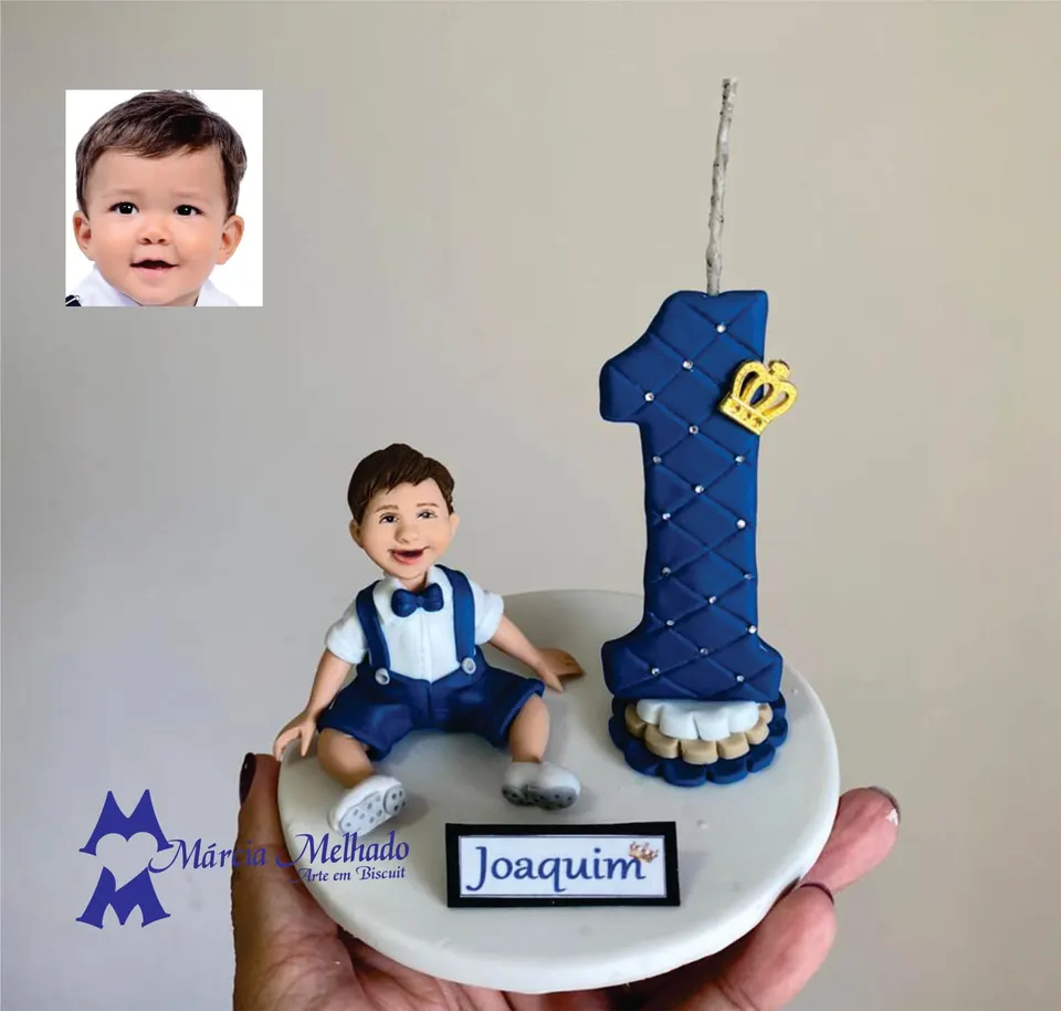 Topo de bolo de 1 ano com menino sentado e número azul com coroa Topo de bolo de biscuit com menino de gravata borboleta e jardineira azul ao lado de número 1 com strass e coroa