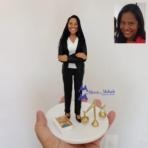 Boneca de biscuit de advogada de blazer preto e braços cruzados, com livro Vade Mecum e balança dourada em base branca