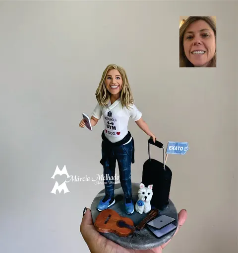 Boneca de biscuit loira de camiseta branca e jeans com celular, ao lado de mala preta, cachorro branco, violão e notebook