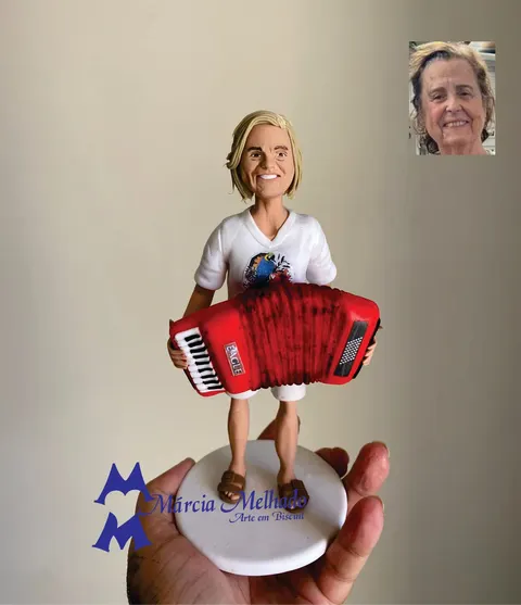 Boneca de biscuit de senhora loira sorrindo e tocando uma sanfona vermelha, com camiseta branca estampada com arara