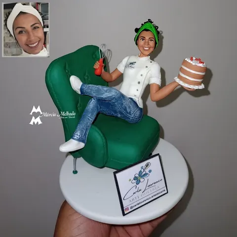 Confeiteira de biscuit de dólmã branca e turbante verde sentada em poltrona verde segurando bolo e batedor de arame