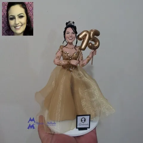 Boneca de biscuit de debutante com tiara, vestido dourado bordado e saia de tule segurando balão dourado com o número 15