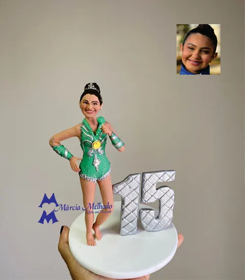 Boneca de biscuit ginasta com collant verde e prata, medalha dourada e coque com tiara, ao lado do número 15 prateado