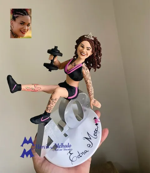 Boneca de biscuit de mulher fitness tatuada com tiara, top e shorts pretos com rosa e halter, sentada no número 40